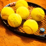 Gros plan de balles de tennis posées sur une raquette sur terre battue