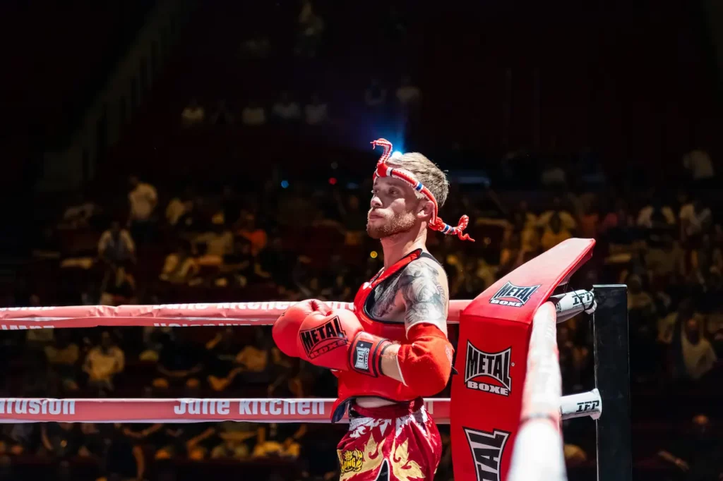 Combattant en tenue rouge appuyé dans son coin sur le ring pendant un gala de boxe à Montauban.