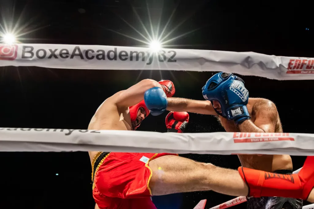 Deux combattants échangeant coups de pied et coups de poing sous les projecteurs pendant un combat de kickboxing à Montauban.