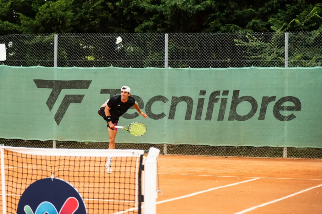Joueur de tennis exécutant un service sur un court en terre battue à Montauban