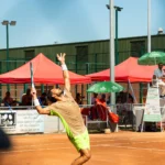 Joueur de tennis au service sur terre battue avec les stands en arrière-plan à Montauban