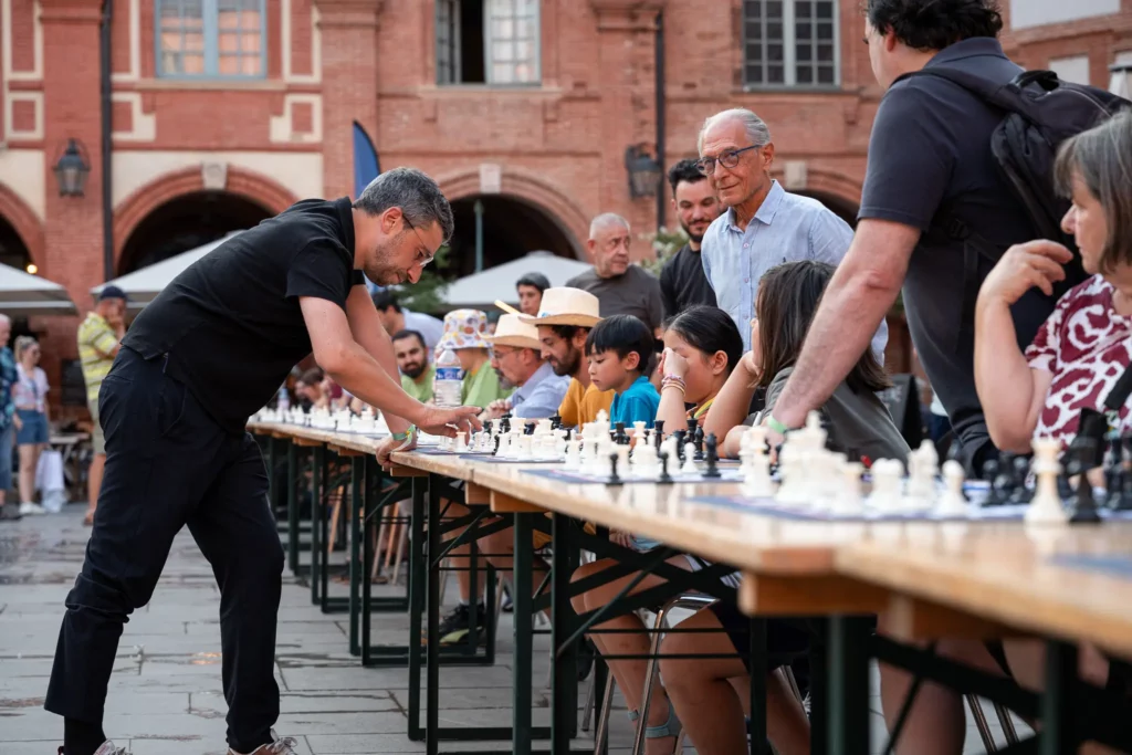 Un joueur se déplace devant une rangée de participants pendant une simultanée d’échecs place Nationale à Montauban